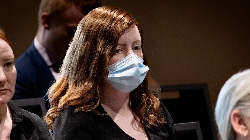 Katrina has red hair and wears a blue surgical face mask