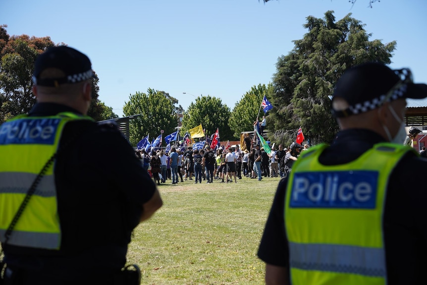 The backs of two police, with a crowd of protesters in the background.