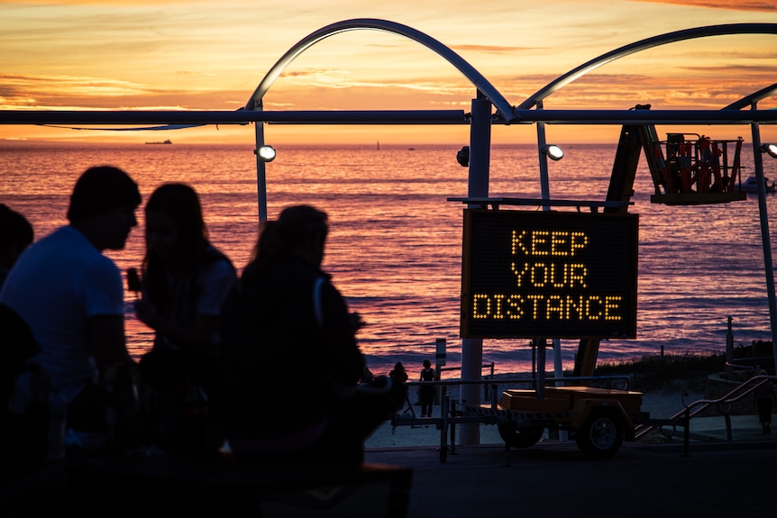 Sun sets over the ocean with a sign saying 'Keep your distance'