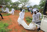 Forensic experts and homicide detectives carry the bodies of suspected members of a Christian cult.