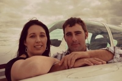 a woman and a man lean on an airplane wing