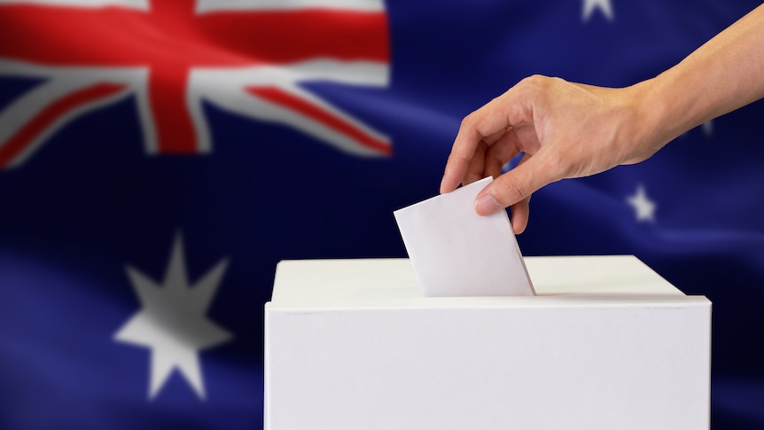 Close up image of human hand inserting a vote into a ballot box, with Australian flag in background.