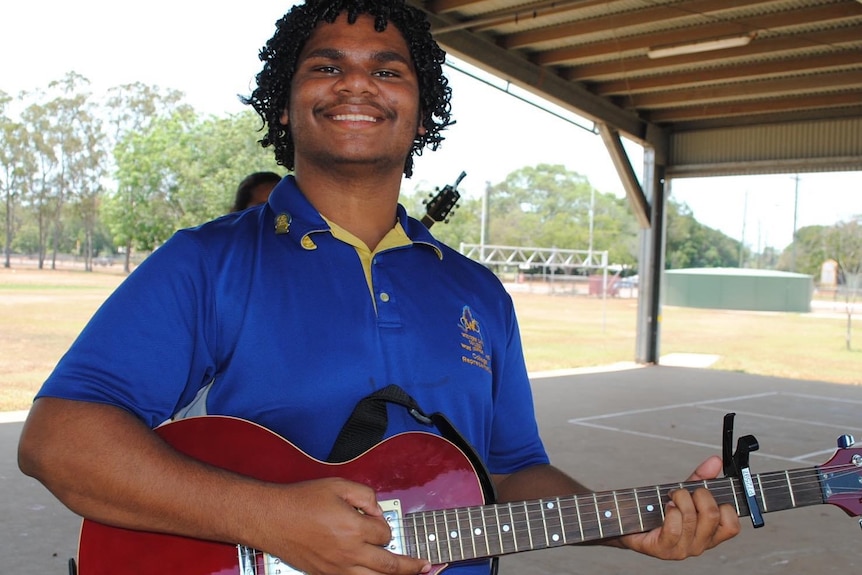 A smiling teenager plays a guitar.
