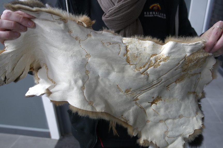 a lady holding up a possum skin with designs burned into it 