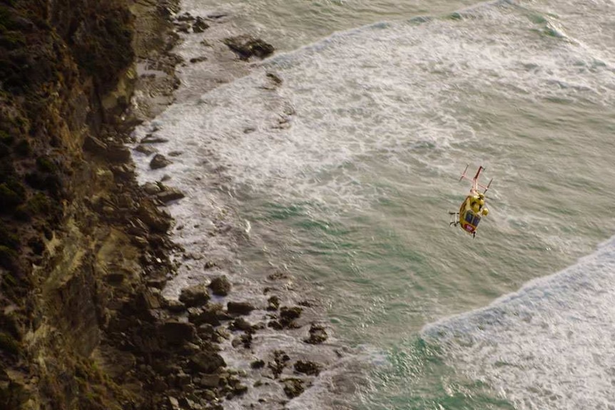 Helicopter flying low over rocky coastline.