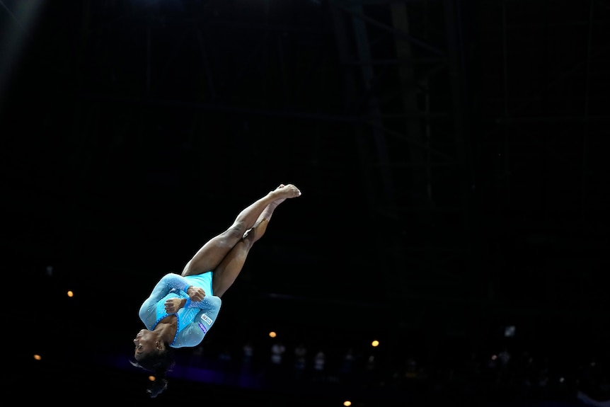Simone flies through the air, with her body pulled taught and her feet in the air and her head heading towards the ground.
