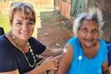Two women sitting next to each other, with one pointing to the vaccine mark on the other's arm.