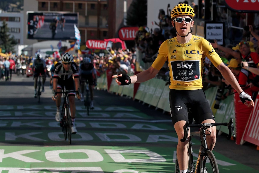 Geraint Thomas celebrates with his arms aloft, his opponents in the distance behind him.
