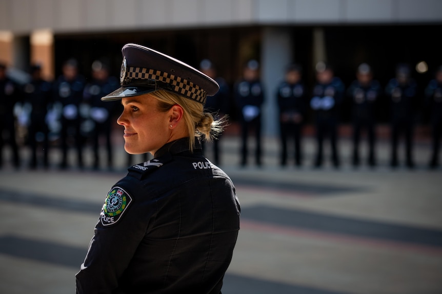 A female police officer stands in the foreground with more officers lined up in a guard of honour