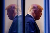 A side on profile of Trump looking downcast is reflected behind him