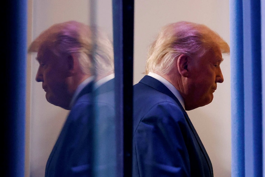 A side on profile of Trump looking downcast is reflected behind him