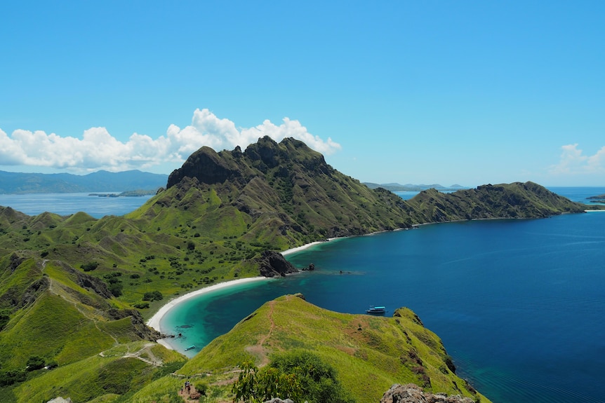 Bright green tropical  mountains shown from above next to a bright blue cove. 