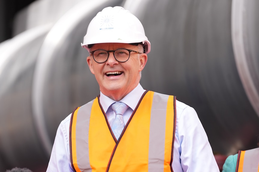 Anthony Albanese laughs while wearing a hard hat and orange high-vis vest.