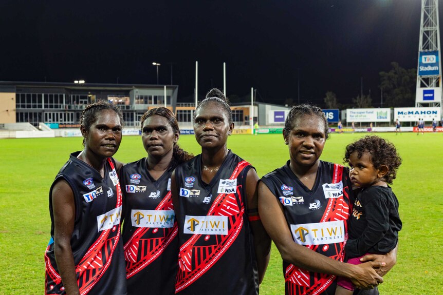 Four Tiwi Bombers and a young child stand on the turf of TIO oval.