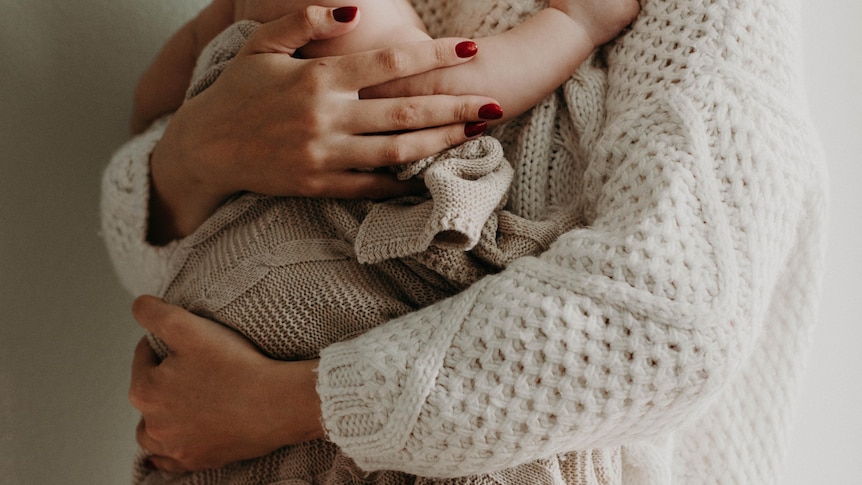 Mother wearing knitted jumper cradles baby in blanket.