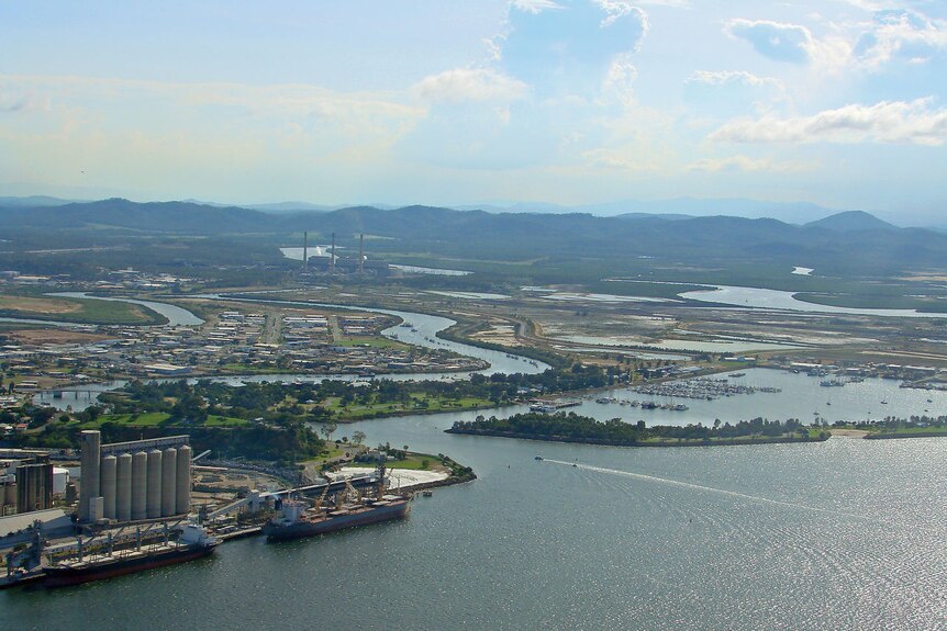 An aerial shot of a seaside town by a river and lake inlet, with a shipping port and large silos at the port.