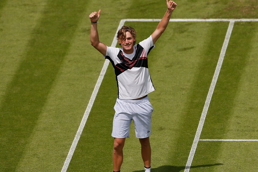 Max Purcell holds both thumbs up in celebration while standing on a grass tennis court