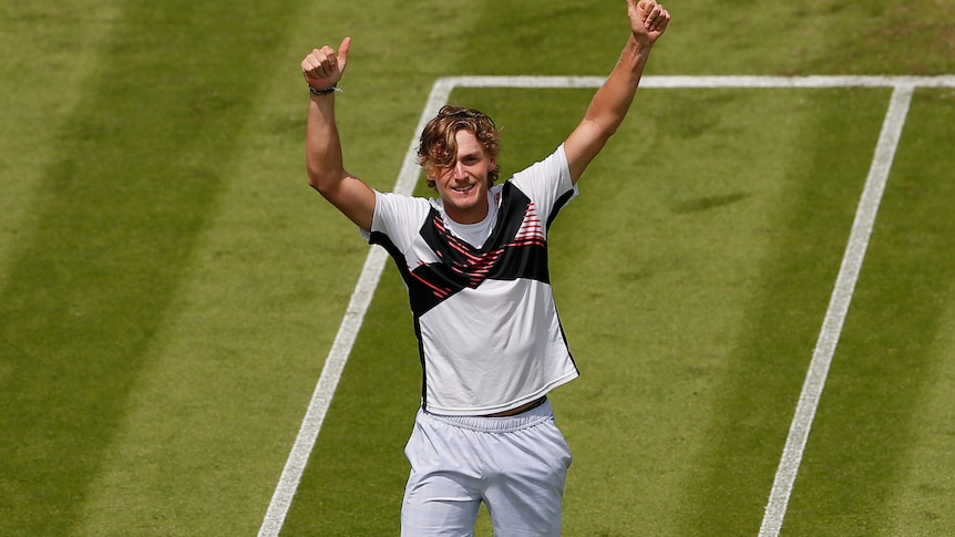 Max Purcell holds both thumbs up in celebration while standing on a grass tennis court