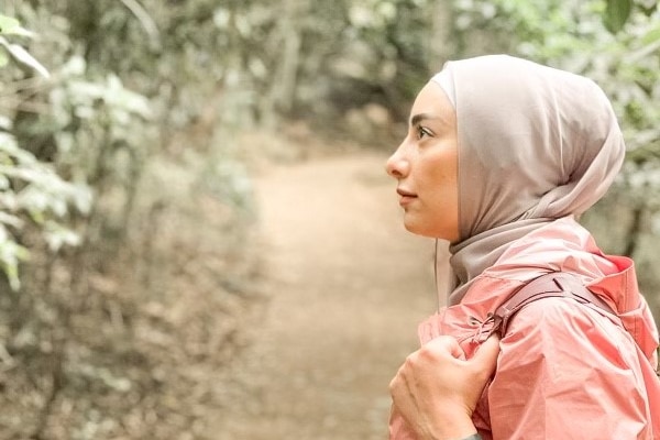 A side profile photograph of Aisha, who wears a headscarf, with trees in the background.