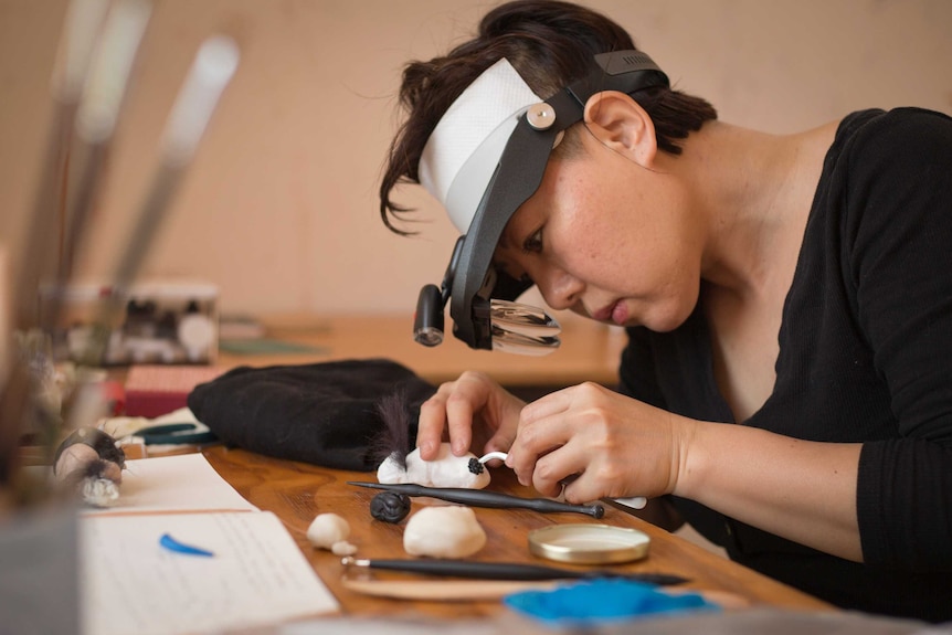 A woman wearing a magnifying glass headband working on a piece of art