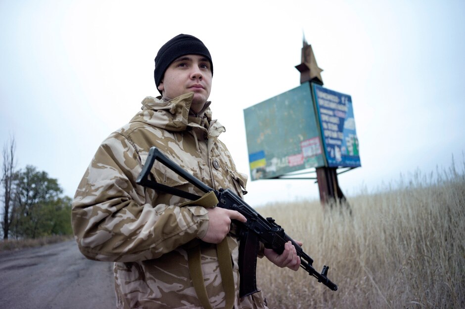 A Ukrainian soldier stands guard on the outskirts of Mariupol, a rusting Soviet-era billboard behind him.