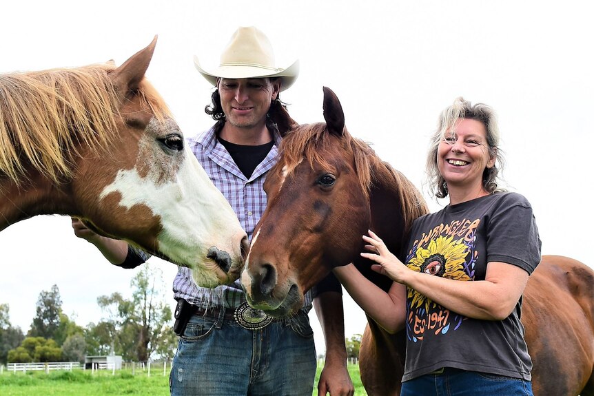 A couple smiling with some horses.
