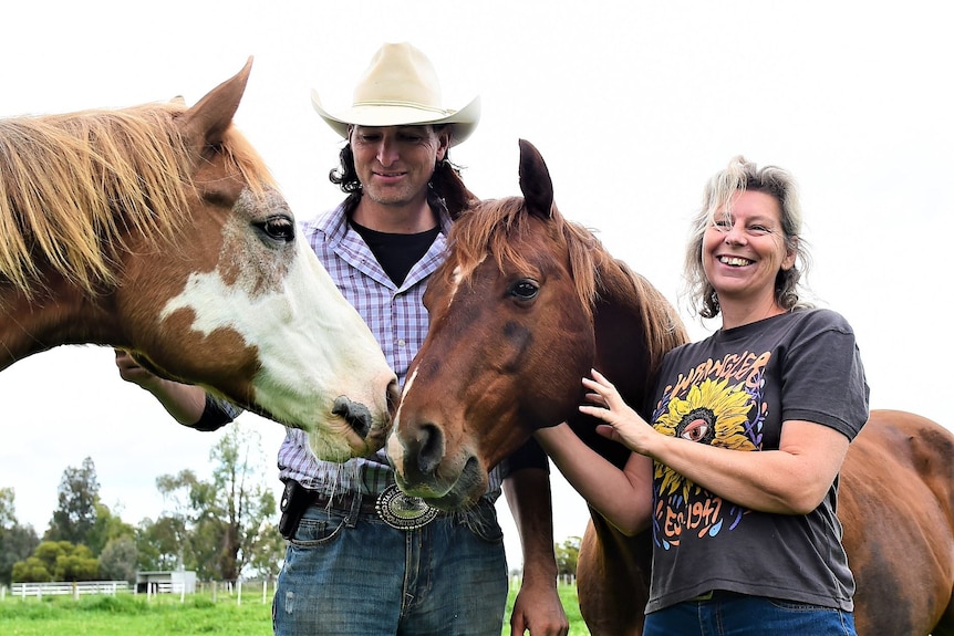 A couple smiling with some horses.