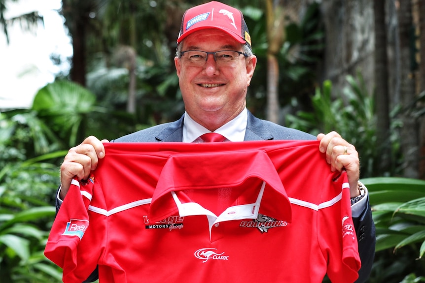 A man in a suit with a Dolphins cap on and holding a jersey.