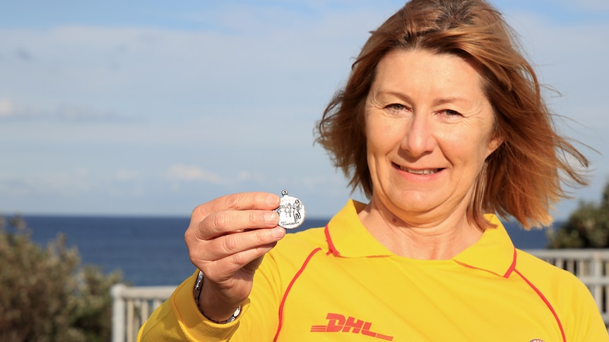 A women stands in a surf life saving uniform and hold a medallion up to the camera