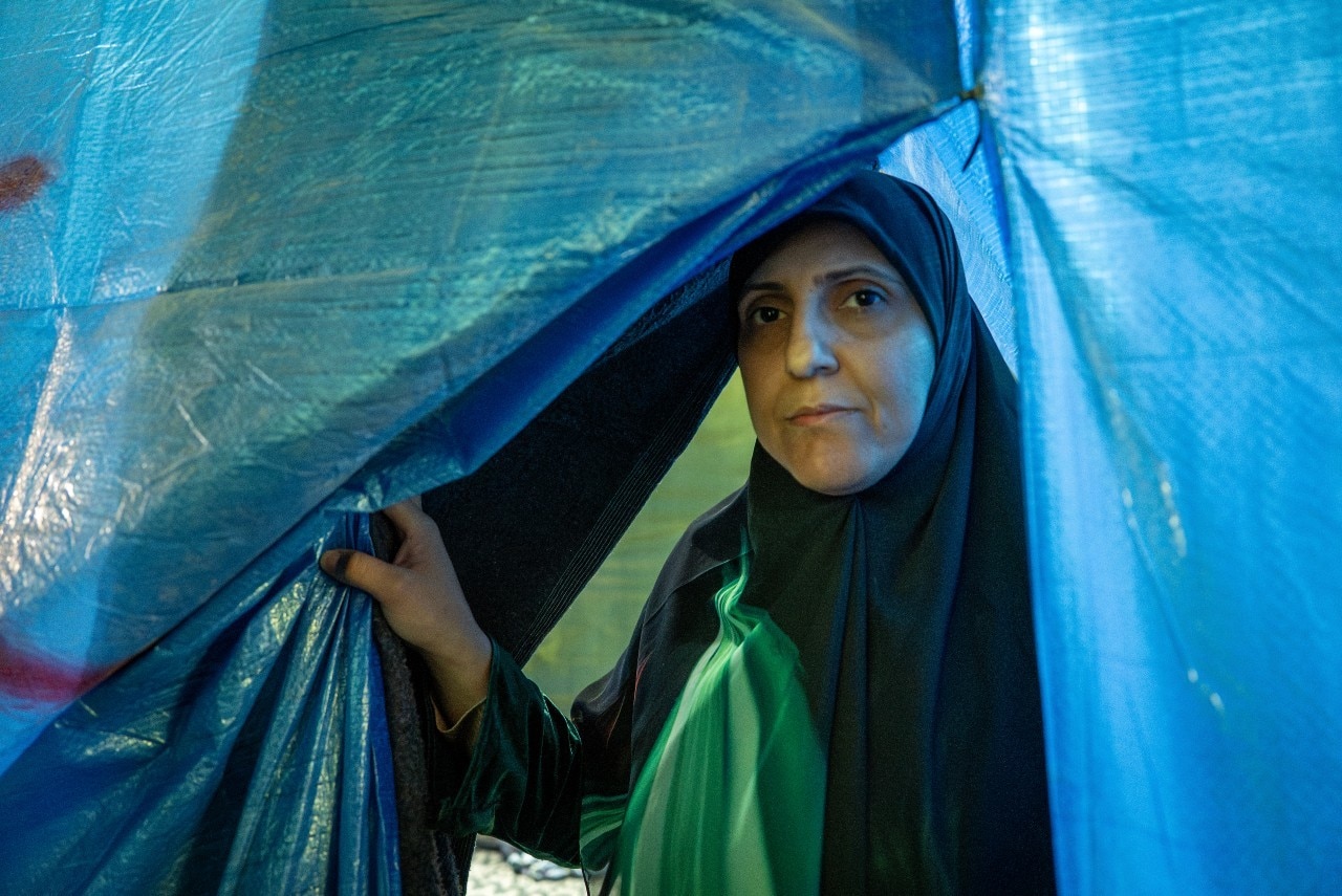 A woman peering through the side of a tent.