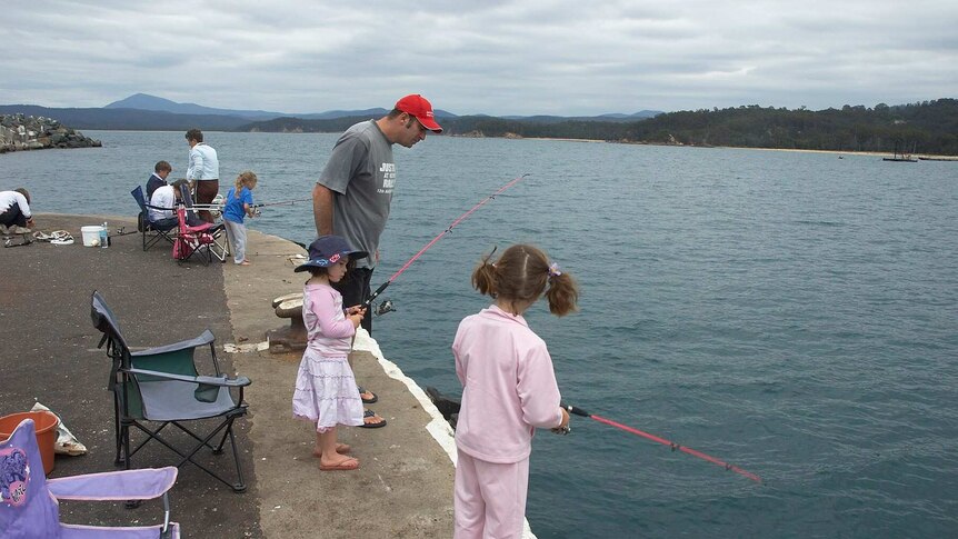 Three little girls, one dressed in pyjamas, fishing with pink rods at Eden's Snug Cove wharf
