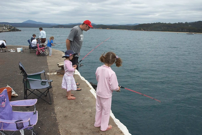 Three little girls, one dressed in pyjamas, fishing with pink rods at Eden's Snug Cove wharf