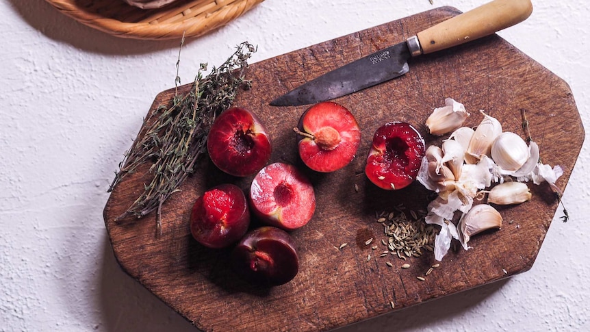 Plums and garlic on a board for chicken tray bake with lemon and thyme recipe