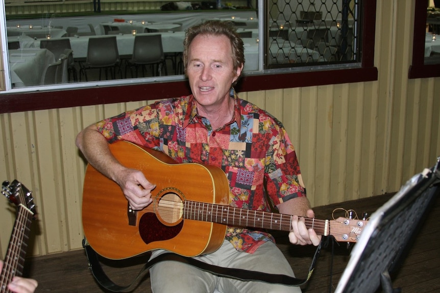 Man wearing a colourful shirt playing a guitar. Picture from around 2009.