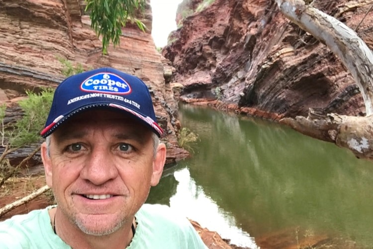 A man in a blue cap stands adjacent a water-filled rocky gorge 