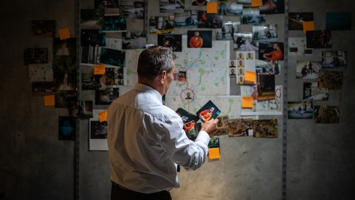 Rear view of a police detective looking pictures in front of the wall with map, and searching for a lead on his case