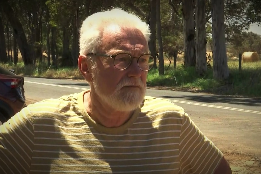 Un homme plus âgé avec des lunettes se tient au bord de la route