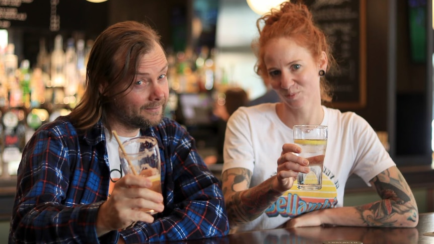 Man and women raise their glasses in a pub, smiling at the camera