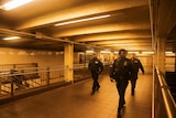 Three officers walk in an empty area of the train station under a warm light.