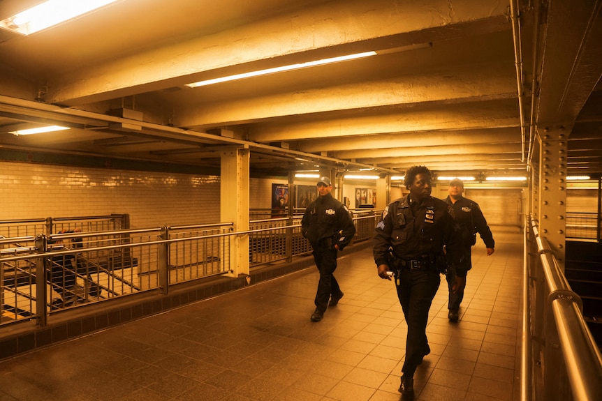 Three officers walk in an empty area of the train station under a warm light.