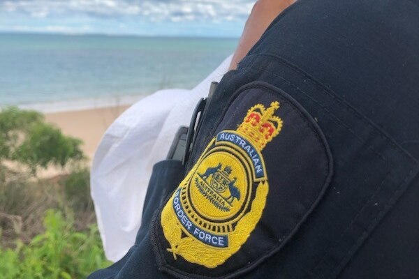 A man looks over the water, with an Australian Border Force badge on his arm