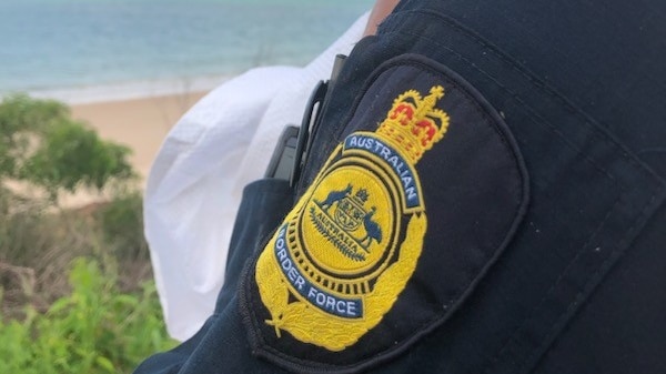 A man looks over the water, with an Australian Border Force badge on his arm
