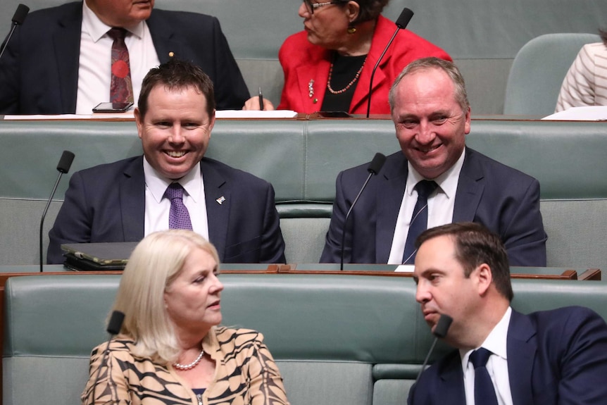 Sitting next to each other in the chamber, the two men are smiling. Other members are in front and behind.