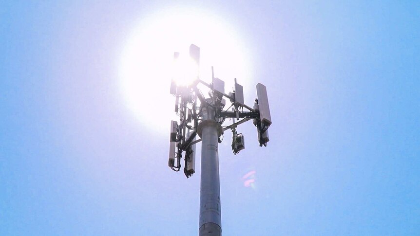The sun blazes behind a mobile phone tower.