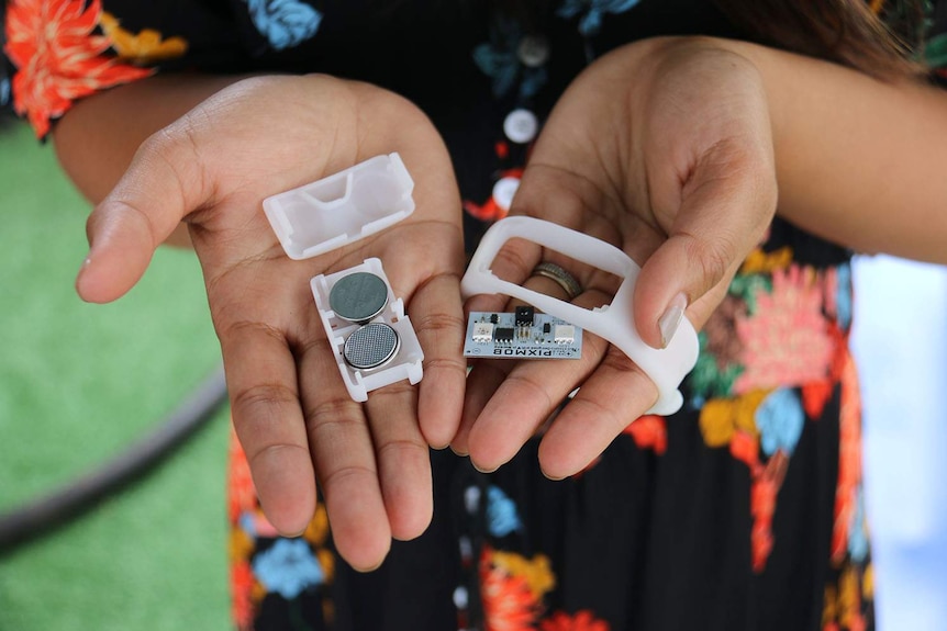 Hands hold a wristband with two button batteries removed that were given out at AFL Grand Final in Brisbane