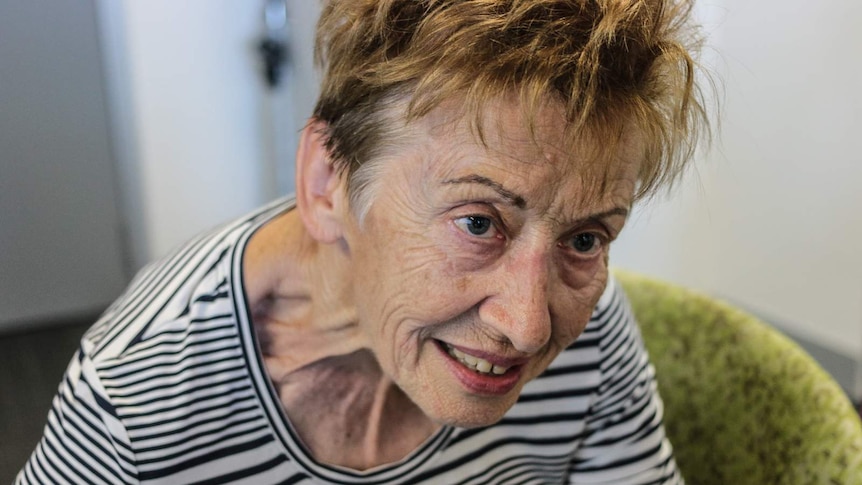 An older woman leans forward and smiles as she sits in a green chair.