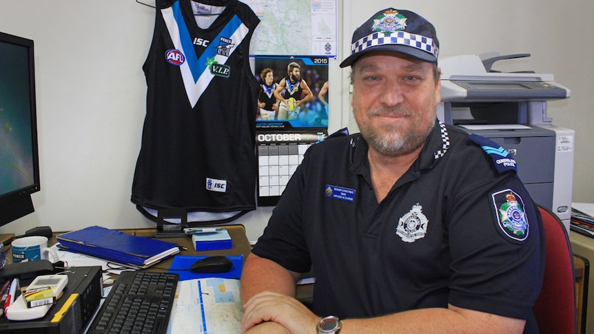 Glenden Senior Constable Brenton O'Brien sitting in his office surrounded by AFL memorabilia