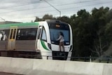 A man clings to the back of a train. Photo taken through car window.