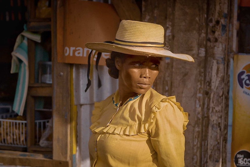 A wsoman wearing a straw hat looks to her left.