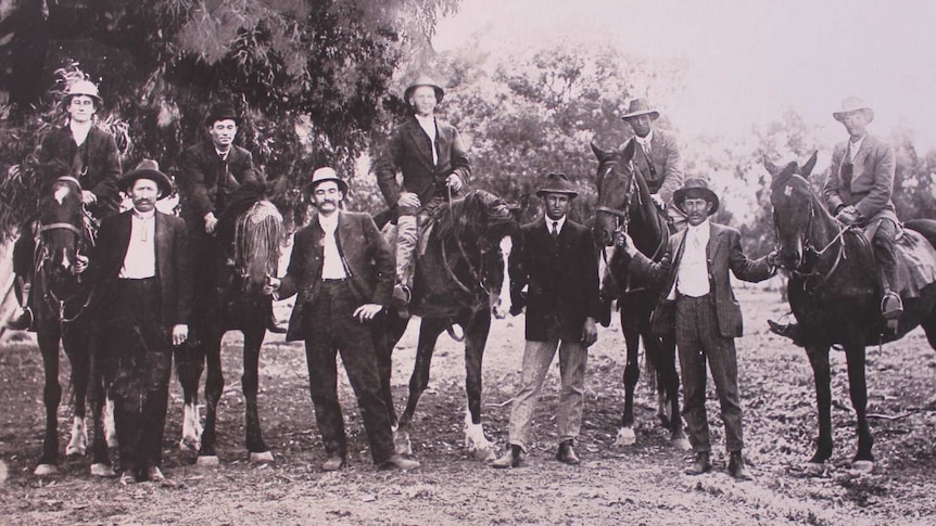 A black and white photo of nine men, five on horseback.